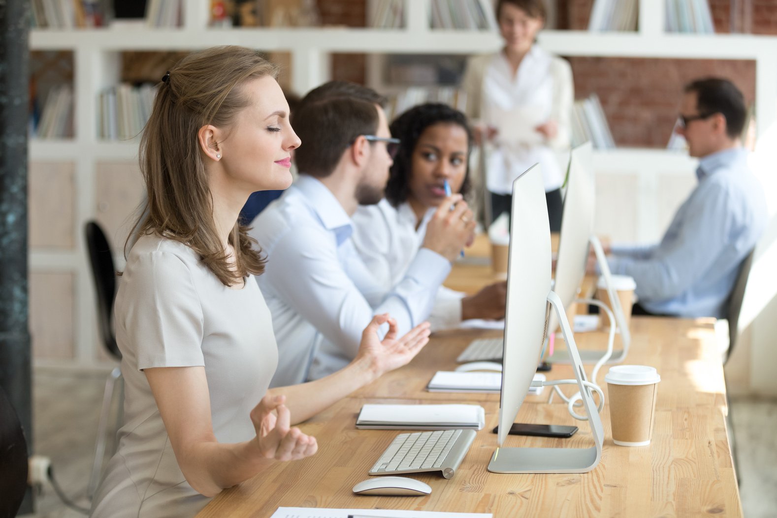 Peaceful female employee meditating at workplace in shared office